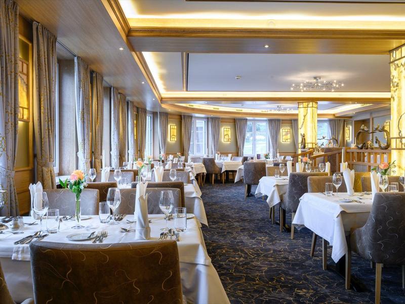 Elegantes Restaurant mit weißen Tischdecken, braunen Stühlen und warmem Deckenlicht.