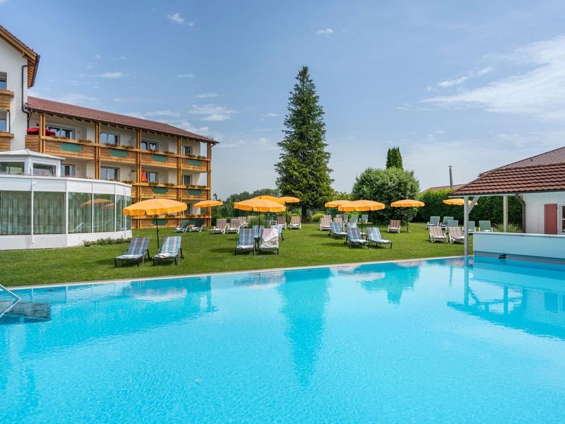 Schwimmbad mit blauer Wasserfläche, gelben Sonnenschirmen und grüner Rasenfläche vor Gebäuden.