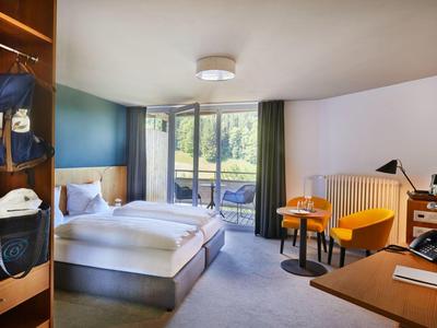 Modernes Hotelzimmer mit Doppelbett, Balkon, gelben Sesseln, Schreibtisch und offenem Schrank.