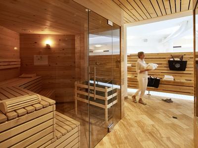 Moderne Sauna mit hellem Holz, Glaswänden und zwei Personen beim Saunieren.