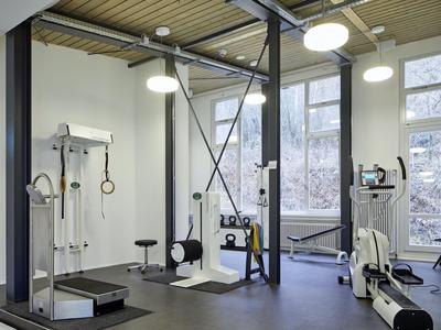 Modernes Fitnessstudio mit Geräten und großen Fenstern in einem hellen Raum.