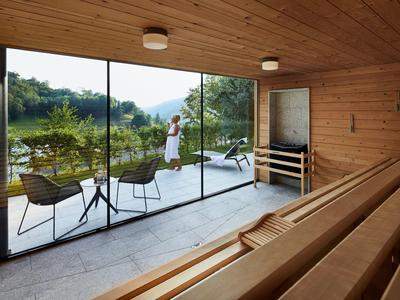 Moderne Sauna mit Holzbänken, großer Glasfront und Terrasse mit Stühlen und Blick ins Grüne.