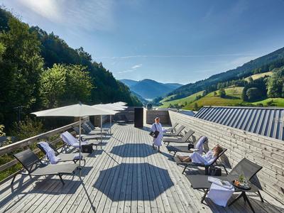 Große Holzterrasse mit Liegestühlen, Sonnenschirmen und Bergblick unter blauem Himmel.