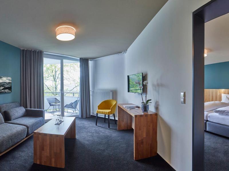 Modern eingerichtetes Wohnzimmer mit Sofa, Holzkommode, Fernseher und Zugang zu einem Schlafzimmer und Balkon.