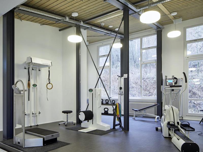 Innenraum eines Fitnessstudios mit verschiedenen Trainingsgeräten und großen Fenstern.