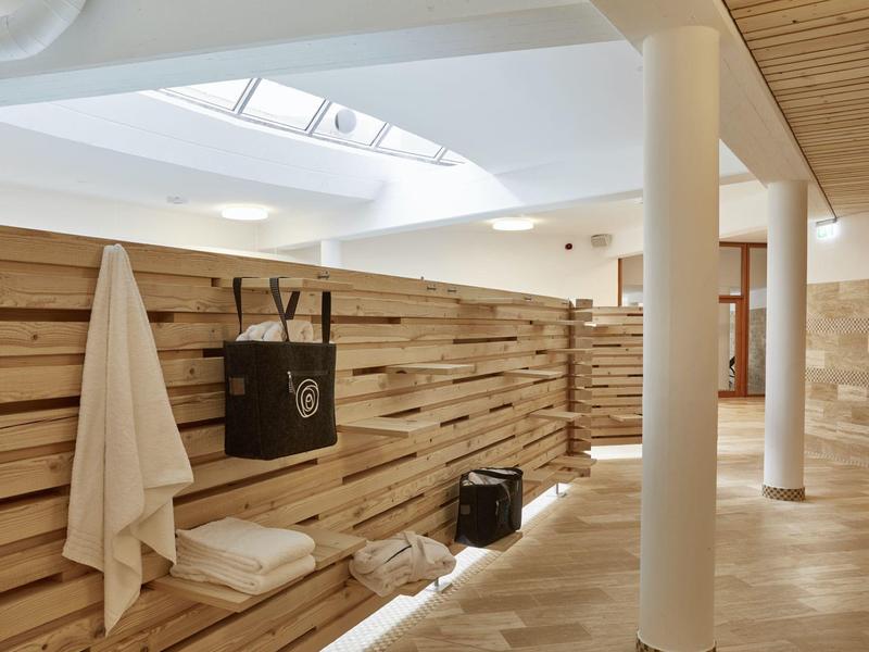 Heller, moderner Saunabereich mit Holzverkleidung, Bänken und Handtüchern an der Wand.