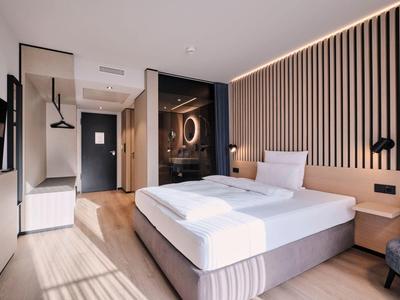 Helles Hotelzimmer mit Doppelbett, Holzvertäfelung, Flachbildfernseher und moderner Beleuchtung.