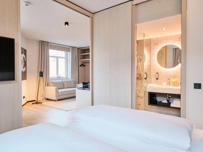 Modern eingerichtetes Hotelzimmer mit zwei Betten, TV, Sofa und Badezimmer mit rundem Spiegel.