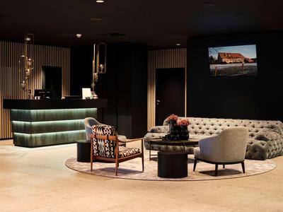 Moderner Empfangsbereich mit rundem Sofa, Sesseln, Tisch und beleuchtetem Tresen in warmem Licht.