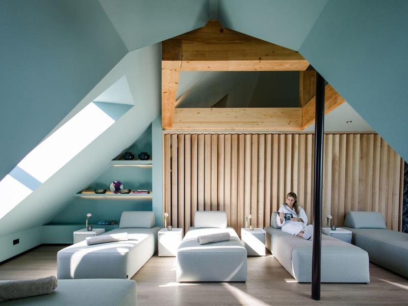 Großer, heller Dachraum mit weißen Sitzmöbeln, Holzvertäfelung und Dachfenstern.
