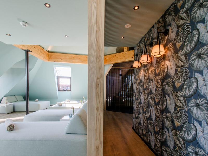 Moderner Wellnessbereich mit Liegen, Holztrennwand und blattgemustertem, dunklem Tapetenakzent.