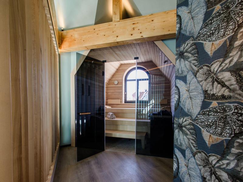 Innenansicht eines Holzraums mit hoher Decke, dunklen Türen und dekorativer Tapete mit Pflanzenmuster.