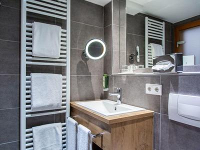 Modernes Badezimmer mit Handtüchern, Waschbecken und beleuchtetem Spiegel in Grautönen.