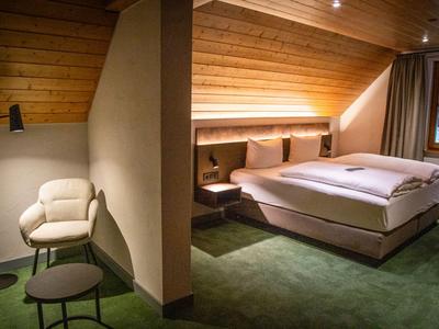 Gemütliches Hotelzimmer mit Doppelbett, Holzdecke und grünem Teppichboden.