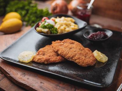 Knusprige Schnitzel mit Beilagen auf einem schwarzen Teller serviert.