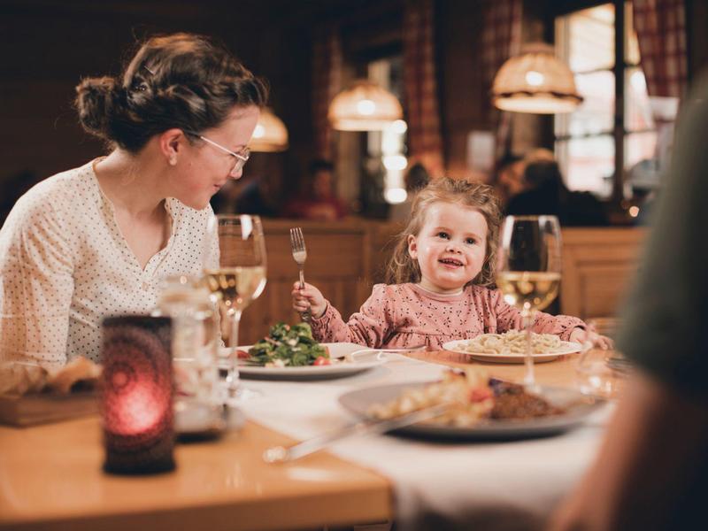 Mutter und kleine Tochter sitzen lachend am gedeckten Esstisch in einem Restaurant.