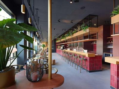 Modernes Hotelrestaurant mit roten Fliesen, Bistrotischen und großen Fenstern.