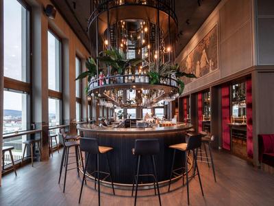 Elegante Hotelbar mit großen Fenstern, rundem Tresen und hohen Stühlen in modernem Ambiente.