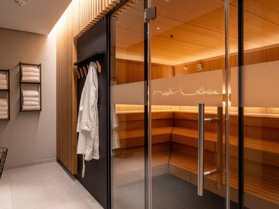 Moderner Saunabereich mit Glastür, Holzverkleidung und weißen Bademänteln an der Wand.