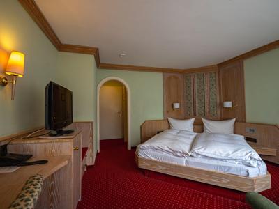 Hotelzimmer mit Doppelbett, Flachbildfernseher, rotem Teppich und Wandbeleuchtung