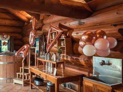 Rustikaler Innenraum mit Holzfass, Ledersesseln und kupferfarbenen Luftballons dekoriert.