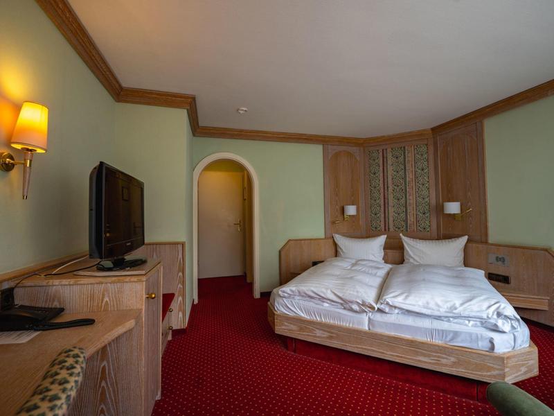 Gemütliches Hotelzimmer mit Doppelbett, Fernseher und rotem Teppichboden.