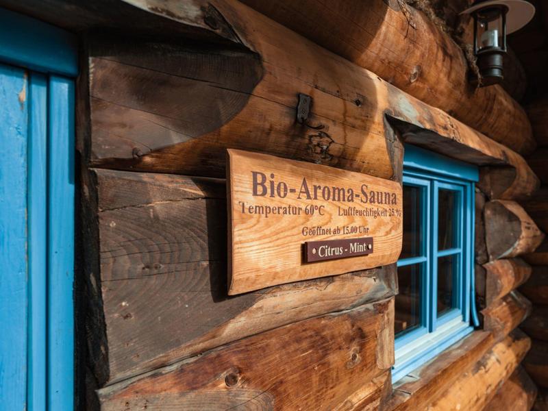 Holzblockhaus mit blauer Tür und Fenster, Schild für Bio-Aroma-Sauna an der Wand.