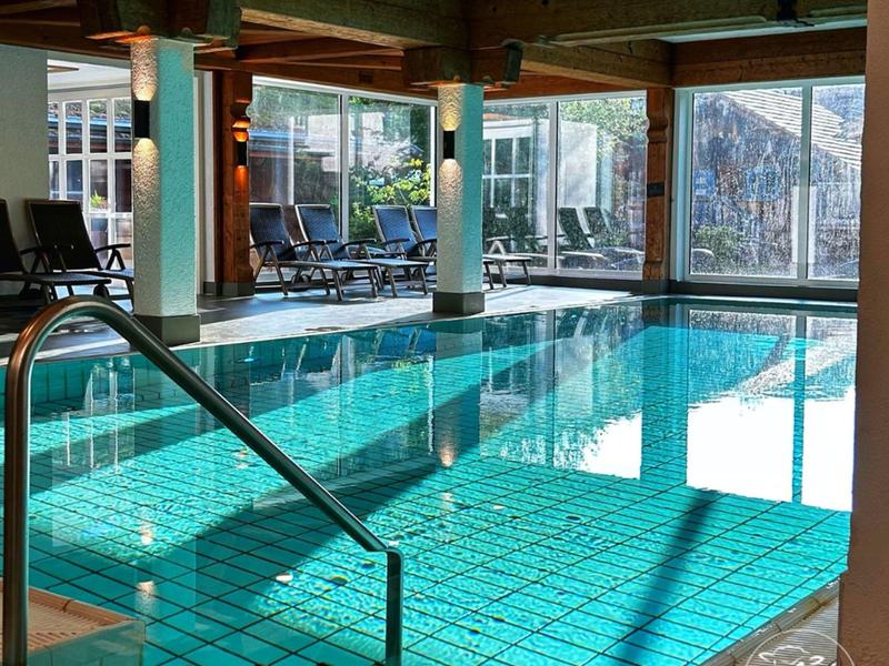 Beheiztes Hallenbad mit Wasserfall und Holzdecke in einem modernen Hotel