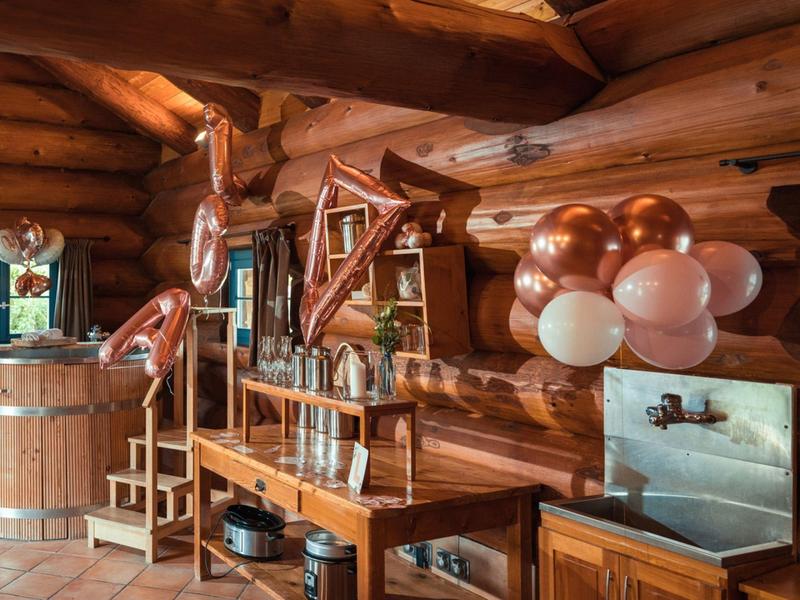 Rustikaler Innenraum mit Holzfass, Ledersesseln und kupferfarbenen Luftballons dekoriert.