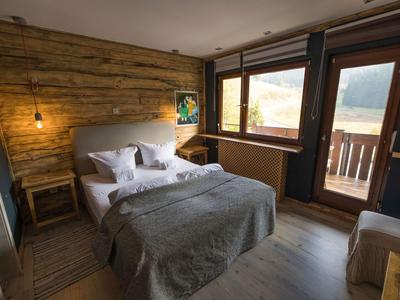 Gemütliches Hotelzimmer mit Holzwänden, Bett, Fenster und Balkon mit Bergblick.