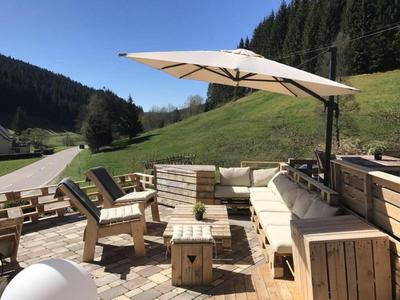 Gemütliche Outdoor-Lounge mit Holzmöbeln und Sonnenschirm in bergiger Landschaft.