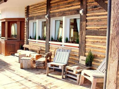 Terrasse eines rustikalen Hotels mit hölzernen Stühlen und Tischen bei Sonnenschein.