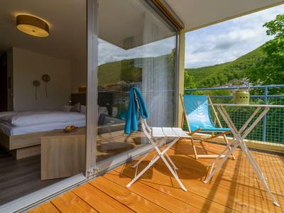 Balkon mit Holzfußboden, zwei weißen Stühlen und Tisch vor einem Schlafzimmer mit Bergblick.