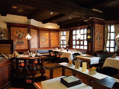 Gemütlicher, rustikaler Gastraum mit Holzbalken, dekorativen Wandbildern und liebevoll gedeckten Tischen.