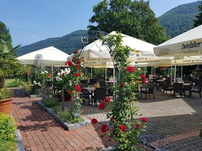 Außenterrasse eines Restaurants mit Tischen unter Sonnenschirmen und Rosenbogen