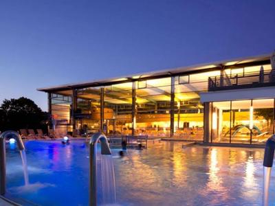 Modernes Hotel mit beleuchtetem Außenpool bei Dämmerung und Glasfassade.
