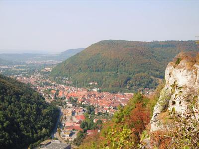 Blick auf eine Stadt im Tal umgeben von grünen Hügeln und felsigen Klippen im Vordergrund.