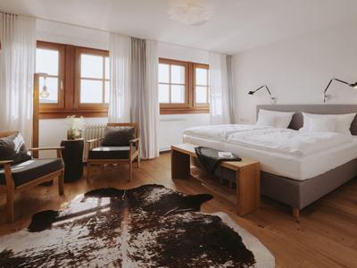 Helles Hotelzimmer mit Doppelbett, zwei Sesseln und Teppich auf Holzboden