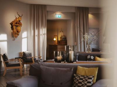 Gemütlicher Hotel-Loungebereich mit Sesseln, Sofas und dekorativen Elementen in warmem Licht.