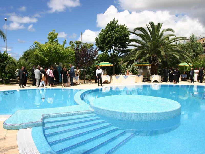 Velký modrý bazén s schody a lidmi v pozadí pod modrou oblohou.