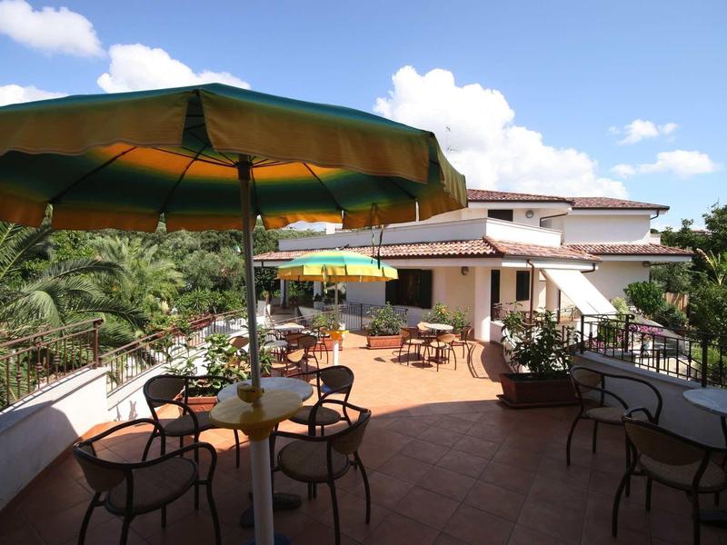 Střešní terasa s stoly, židlemi a slunečníky pod jasnou oblohou.