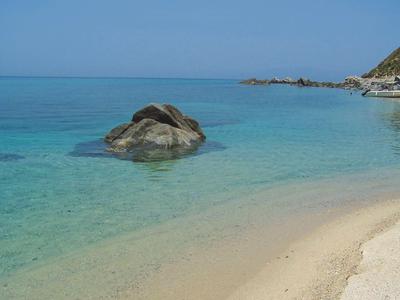 Klares türkisfarbenes Wasser trifft auf einen sandigen Strand mit einem großen Felsen im Wasser.