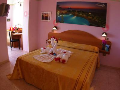 Przytulny pokój hotelowy z dużym łóżkiem i różowymi ścianami, udekorowany ręcznikowymi łabędziami.