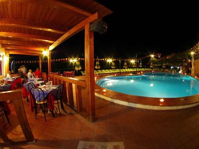 Oświetlony basen i taras hotelowy z gośćmi jedzącymi kolację na zewnątrz.