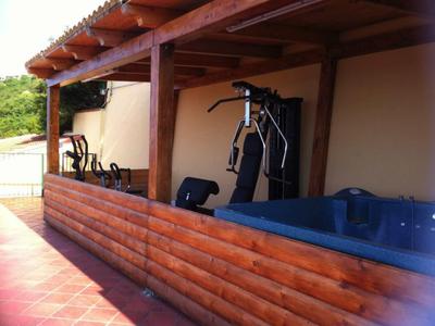 Überdachte Terrasse mit Holzverkleidung, Fitnessgeräten und einem kleinen Whirlpool.