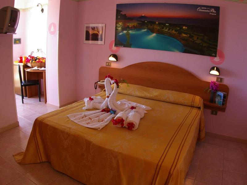 Przytulny pokój hotelowy z dużym łóżkiem i różowymi ścianami, udekorowany ręcznikowymi łabędziami.