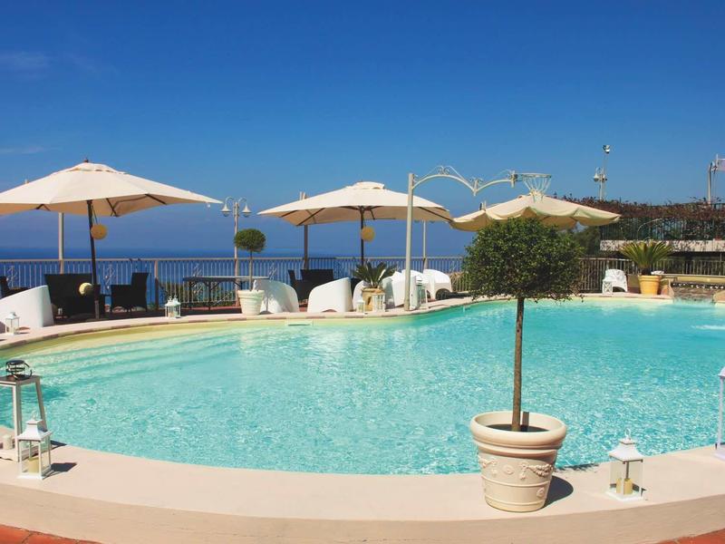 Okrągły basen z parasolami i widokiem na morze pod czystym niebem.