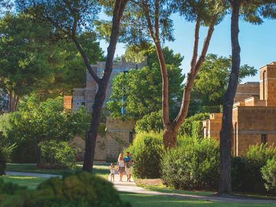 Grüne Gartenanlage mit Bäumen und Menschen vor einem historischen Steingebäude.
