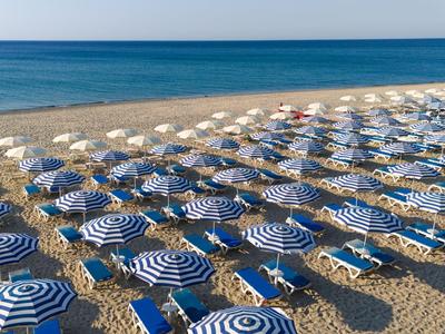 Reihe von blauen und weißen Sonnenschirmen und Liegestühlen an einem Sandstrand am Meer.