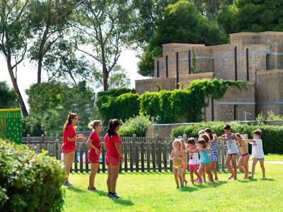 Kinder spielen im Garten vor einem großen, historischen Gebäude aus Stein mit Bäumen im Hintergrund.